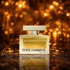  Dolce & Gabbana The One Eau de Parfum gylden amber flacon på mørk gylden glitter overflade med varme amber bokeh-cirkler